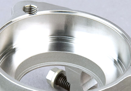 a high-precision machined metal component, likely aluminum given the sheen and apparent lightness. It features a combination of threaded holes suggesting fastening or assembly purposes, smooth internal surfaces likely for a sealing function, and an external mounting flange. The presence of a bolt and washer indicates that it is designed for assembly with other parts. The manufacturing quality is highlighted by the clean finish and sharp detail on the component, which is typical for parts used in specialized industries such as aerospace or automotive, where exact specifications and tolerances are critical.