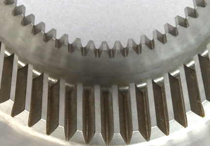 a close-up of the edge of a large, finely machined gear. The individual teeth are well-defined and appear sharp, indicating precise manufacturing. The metal has a matte finish and displays signs of high-quality workmanship. Such gears are typically used in applications where high precision and reliability are required, such as in aerospace or automotive industries. The gear appears to be robust, suggesting it could handle significant loads, which is common in industrial machinery and equipment.