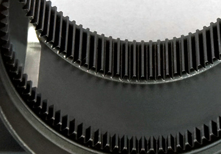 a close-up of a large circular gear with a black center. The gear teeth are precisely machined and arrayed around the outer edge. The quality of the machining is evident by the uniformity of the teeth and the smooth finish of the metal. This gear part is likely to be used in industrial machinery where accurate transmission of torque is essential. The black center might be indicative of a protective coating or a different material used for specific engineering purposes, possibly related to friction, wear resistance, or aesthetic considerations.