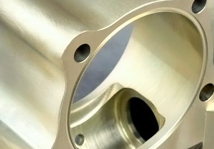 a machined metal part with a smooth, reflective surface. It appears to be a section of a larger mechanical assembly, featuring a cylindrical cavity with a rounded interior profile. There are precisely drilled holes around the perimeter, likely for bolts or rivets to secure this component to others. The meticulous finish and the sheen on the metal suggest high-quality manufacturing processes, such as CNC machining. This component might be used in industries requiring high precision and strength, like aerospace, automotive, or advanced machinery. The craftsmanship indicates a focus on precision and attention to detail.